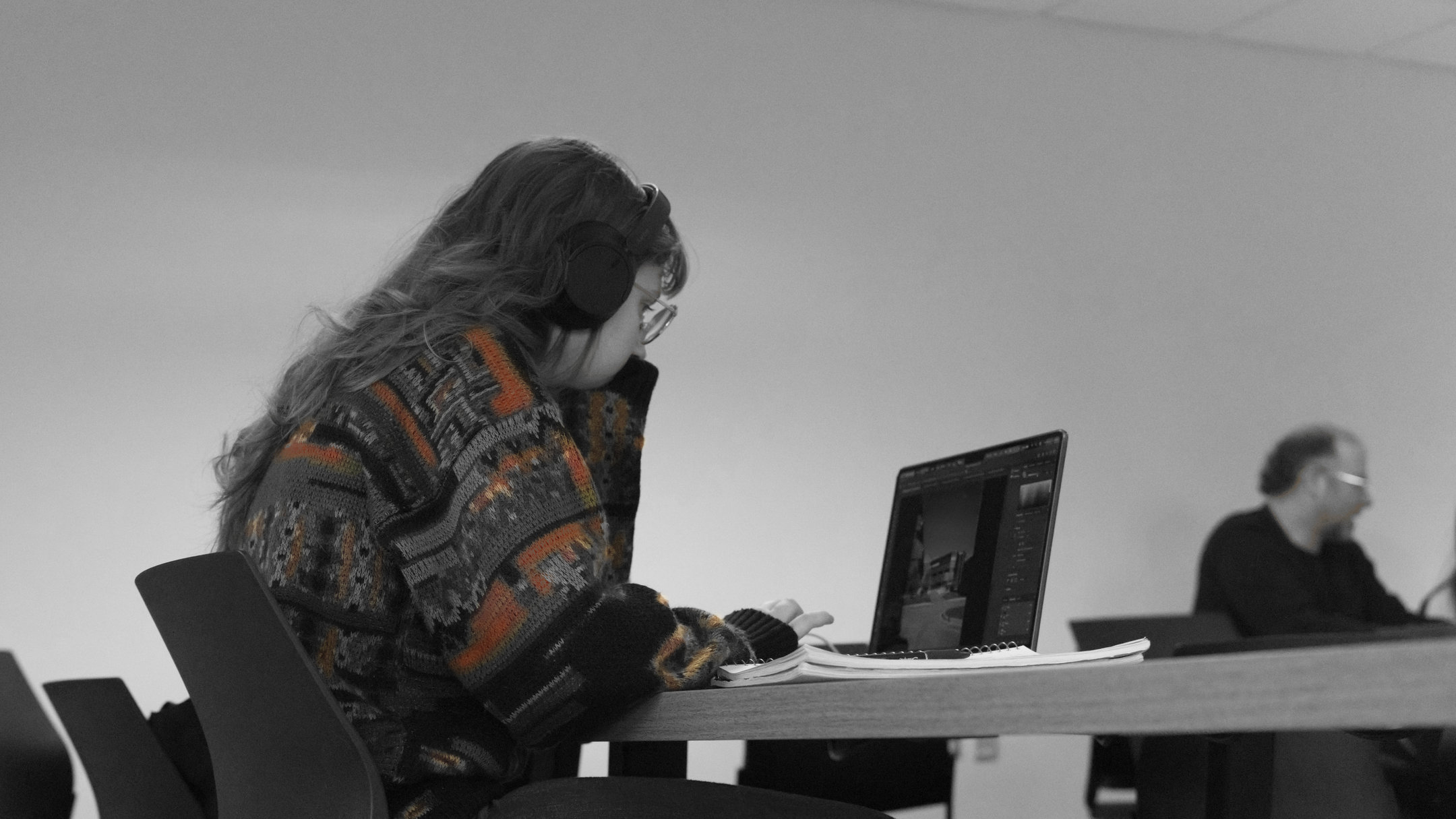 Morning Beginnings, 9:00 AM: in black and white, a student in headphones works on a laptop, the patterned sweater left in colour