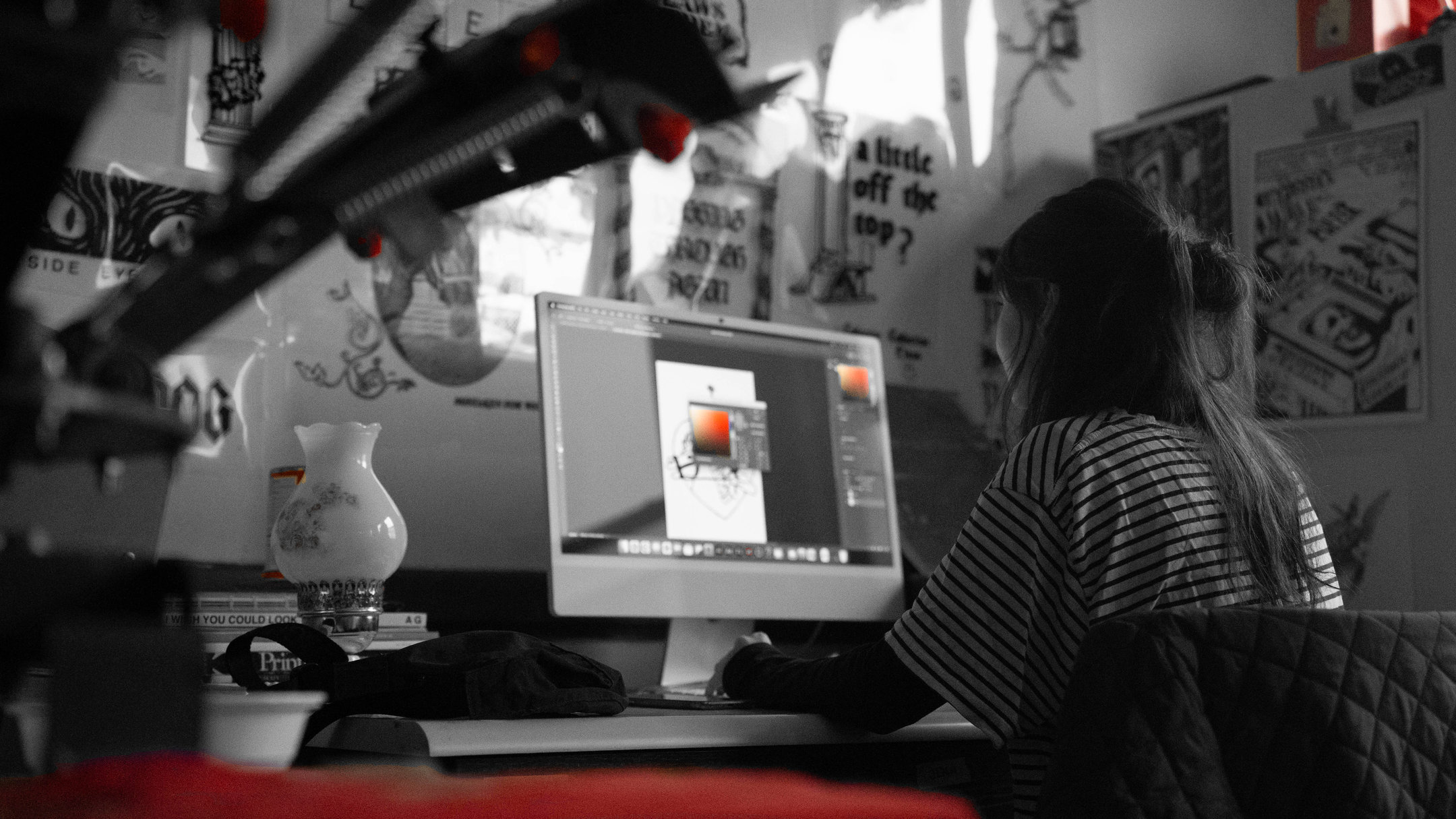 Ideas in Progress, 11:00 AM: a student works on a design at a computer in the print studio, past a screen-printing press with red handles