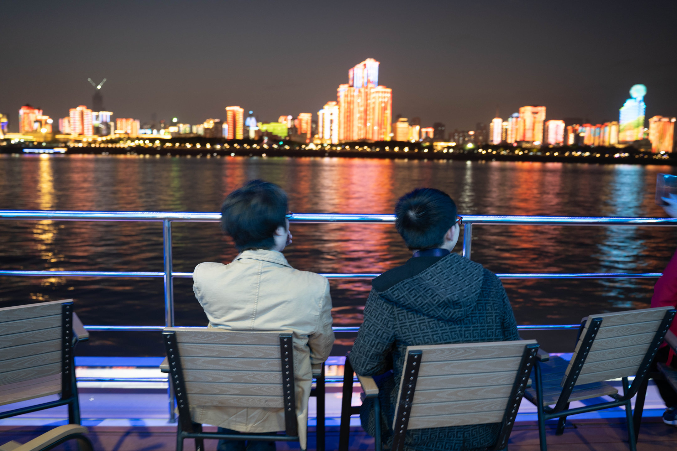 Two passengers on a night ferry looking at the lit shore