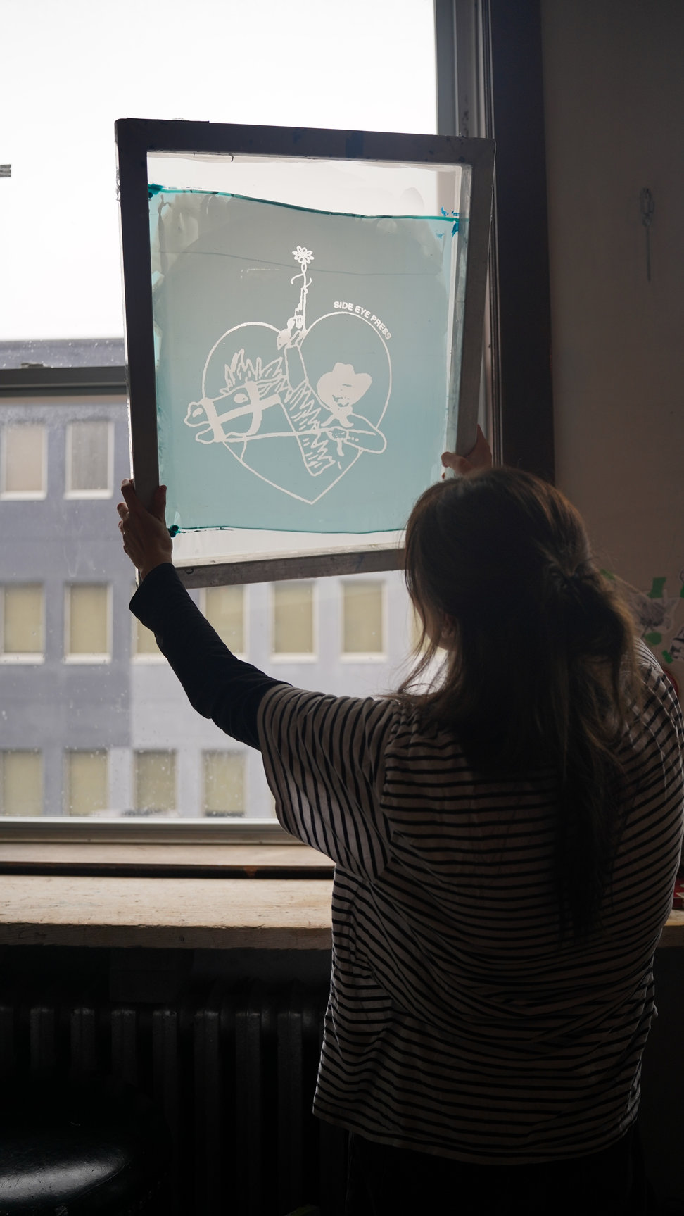 A student holding a silkscreen frame up to a window, in silhouette