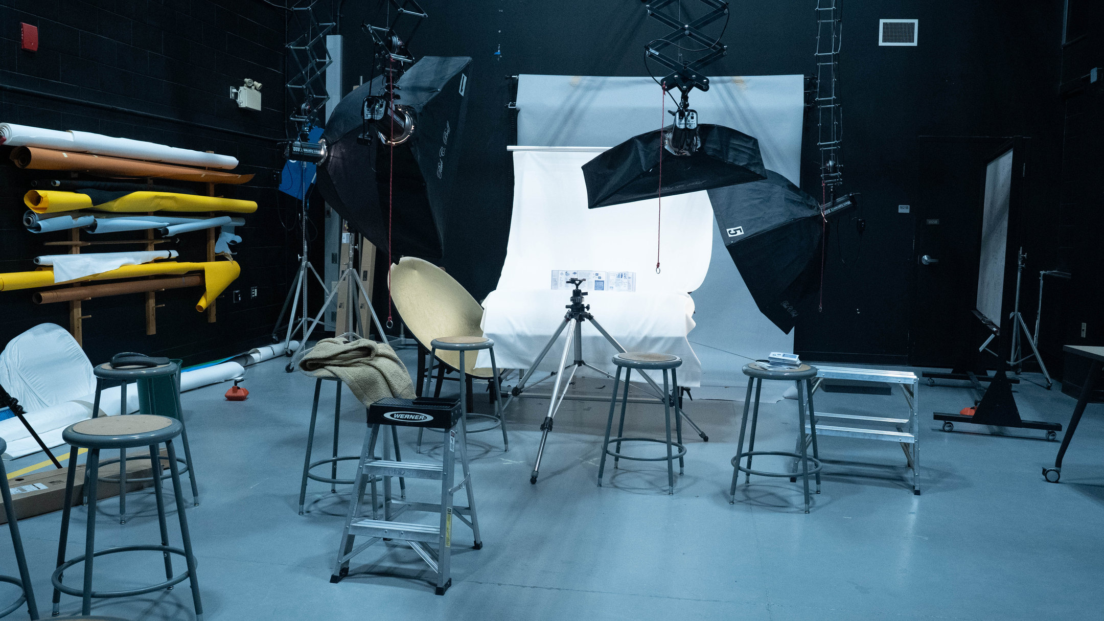The college photo studio: softboxes on booms over a white sweep with the zine on it, a gold reflector, stools and a tripod